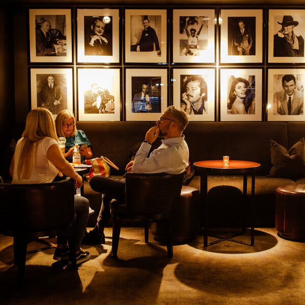 Three people sit at a table in a bar. Along the wall behind them are photographs of movie stars. 