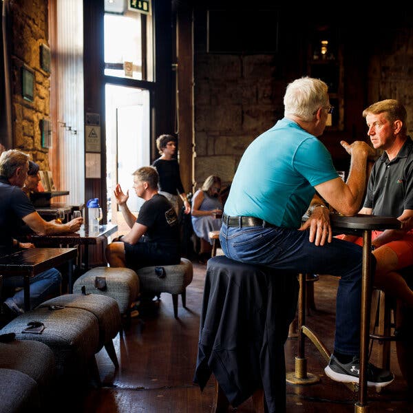 Men sit at low and high tables in a darkly lit room. 