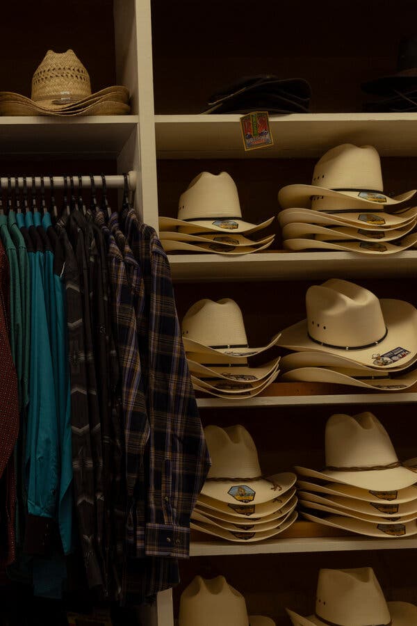 A rack of long-sleeved Western shirts is surrounded by shelves with stacks of straw hats and cowboy hats.