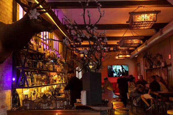 A bar decorated with taxidermy, white flowers and Western-looking square lights. A group of people sitting at one of the tables looks at menus, and at the far end of the bar, a person is sitting on a stool with elbows on the bar.